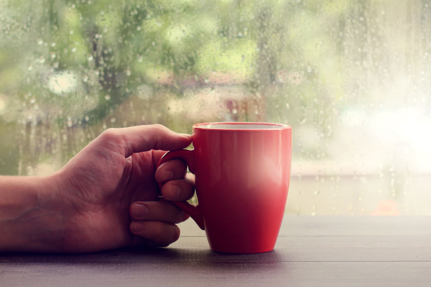 hand grasping cup infront of rain soaked window
